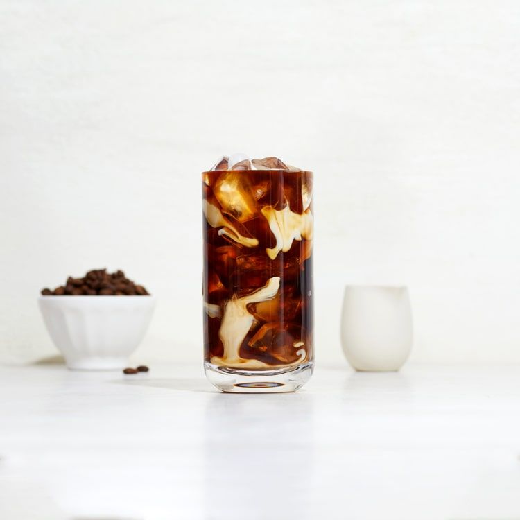 a glass of iced coffee with creamer mixing through it
