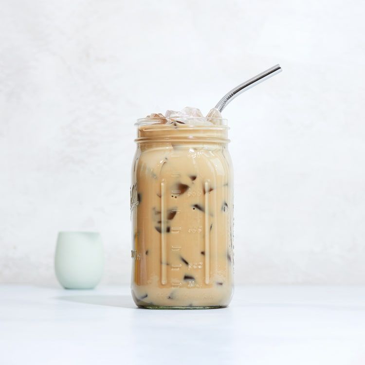 a mason jar with iced coffee and creamer in it