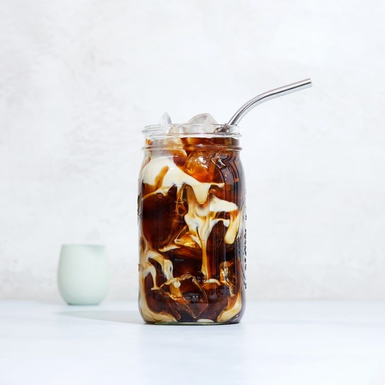 a mason jar with iced coffee and creamer mixing in it