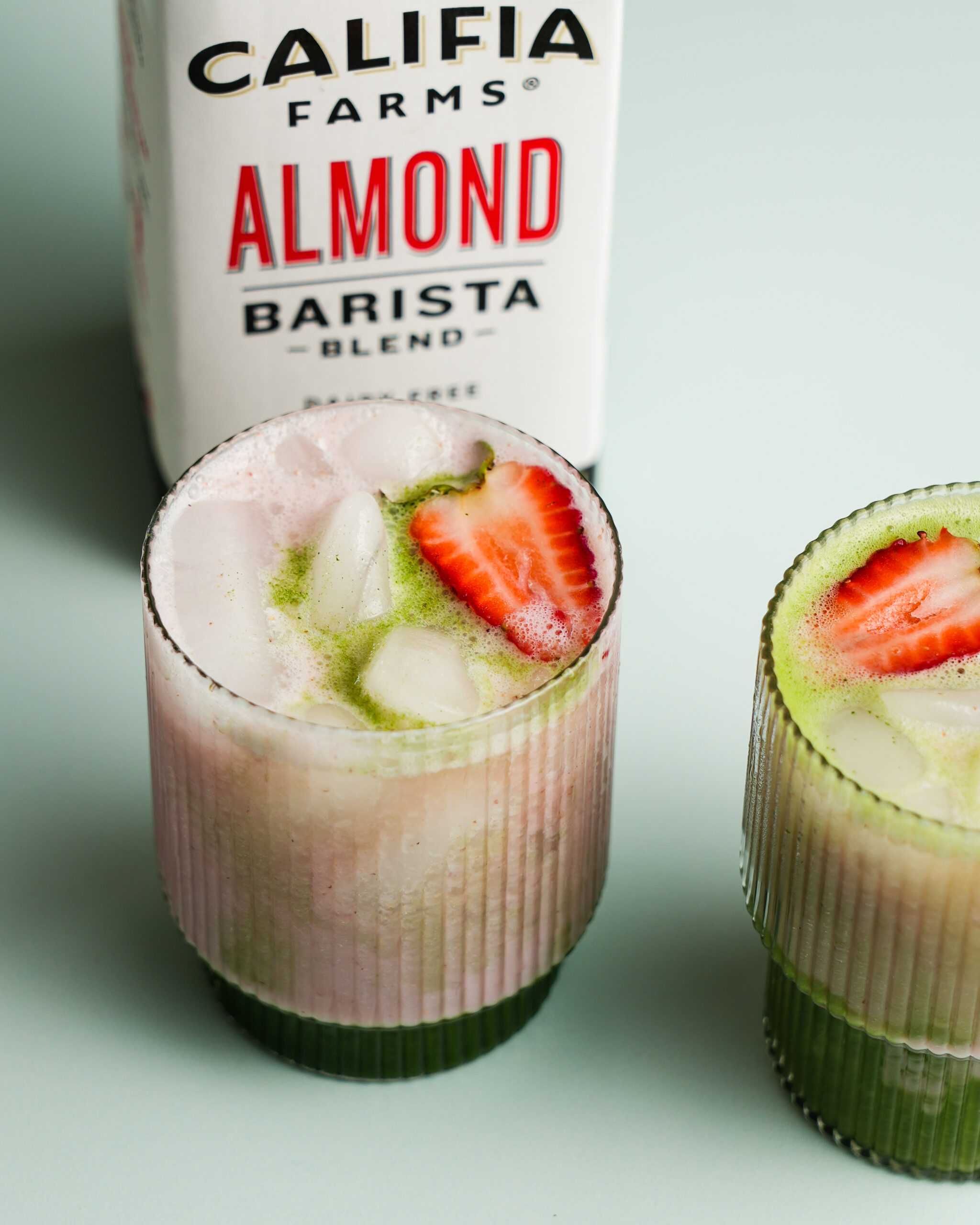 An iced strawberry matcha latte is shown at the forefront of the image, with Califia Farms Almond Barista Blend in the background.